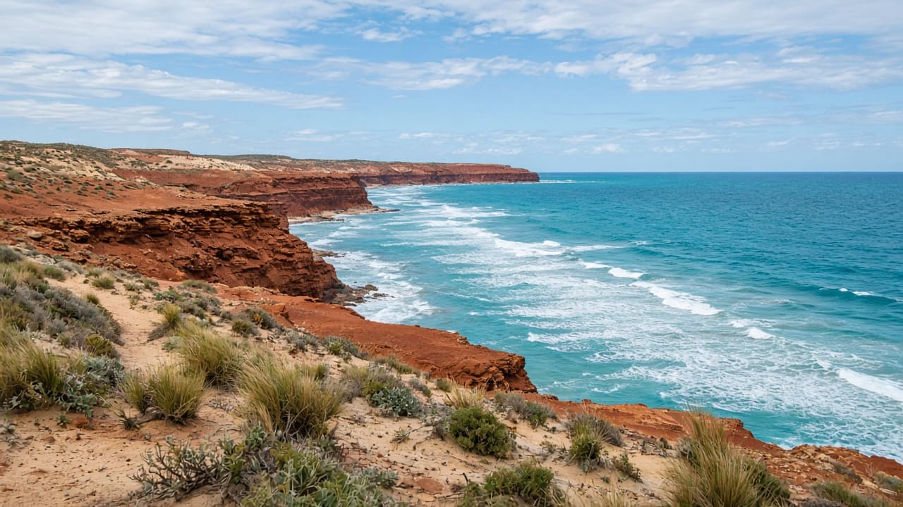 Red cliffs meeting turquoise ocean along an empty Western Australian coast